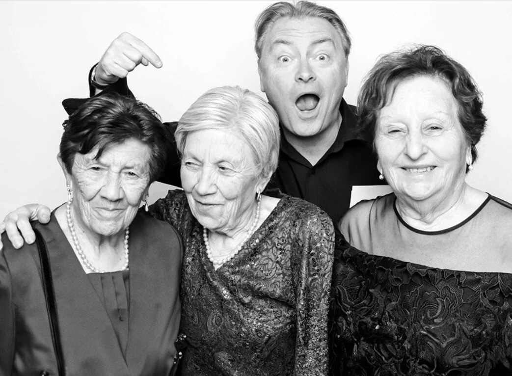 John Warren laughing in a photo booth with three Nonnas