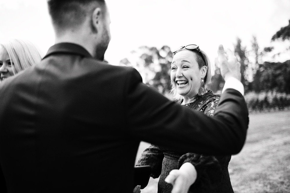 A woman with glasses on her head smiling and talking to a man in a suit outdoors during the daytime. Other people are partially visible in the background.