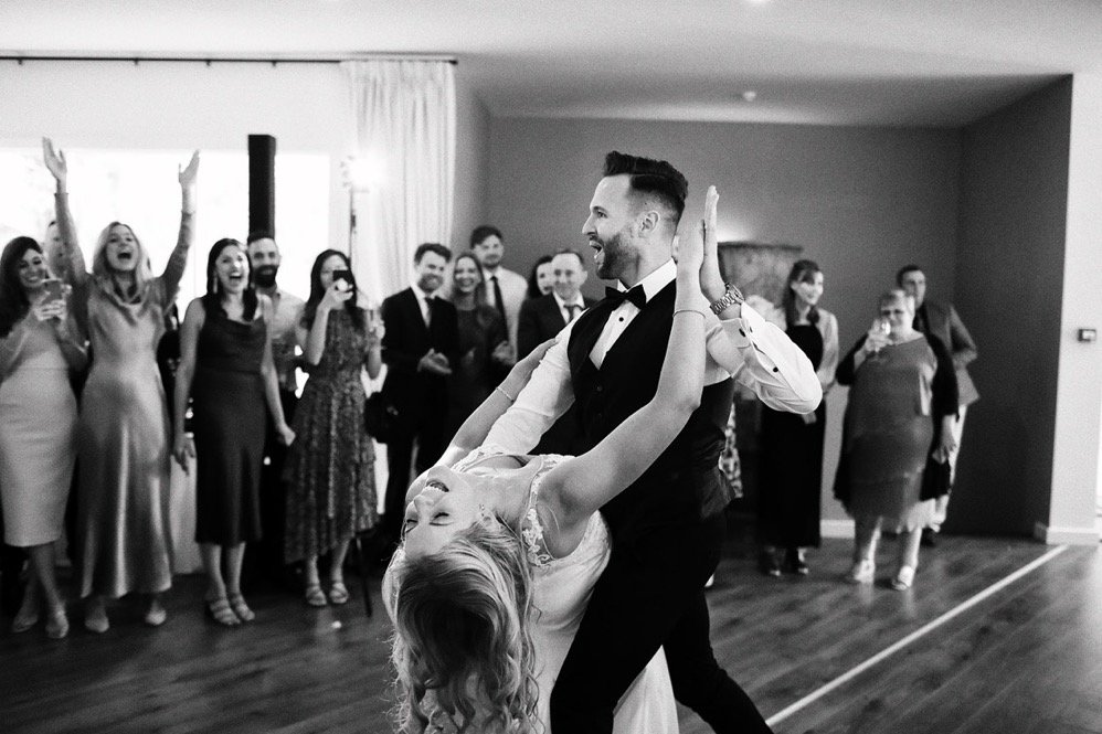 A couple is dancing closely at a wedding reception with guests watching and celebrating around them.
