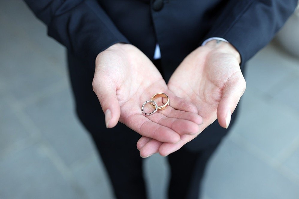 Person in a dark suit holding two wedding rings, one gold and one silver, in open hands.
