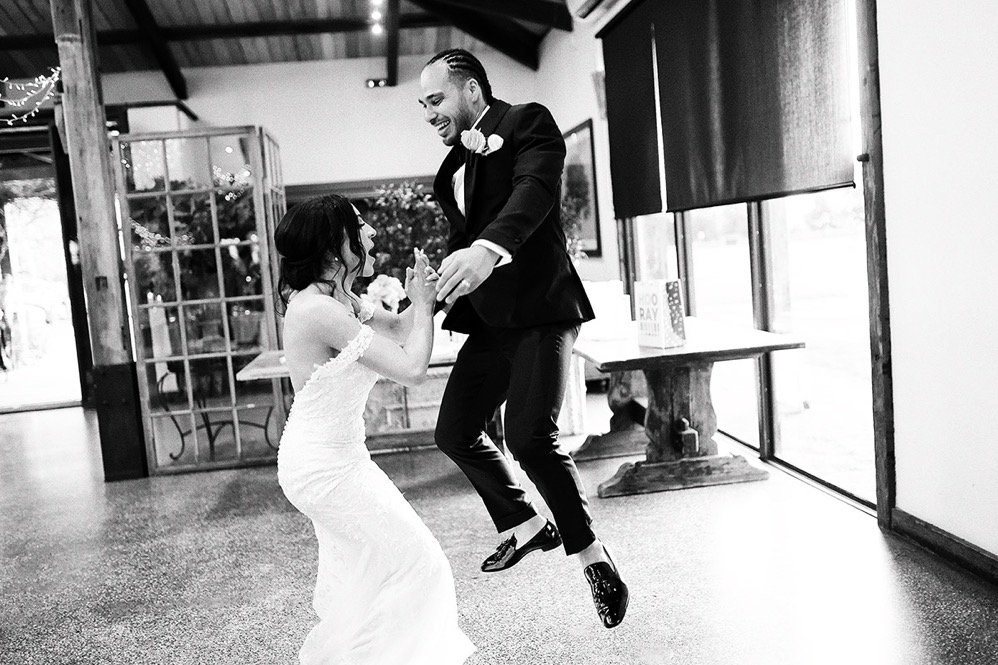 A bride and groom dancing at their wedding reception, smiling and holding hands in a joyful moment.