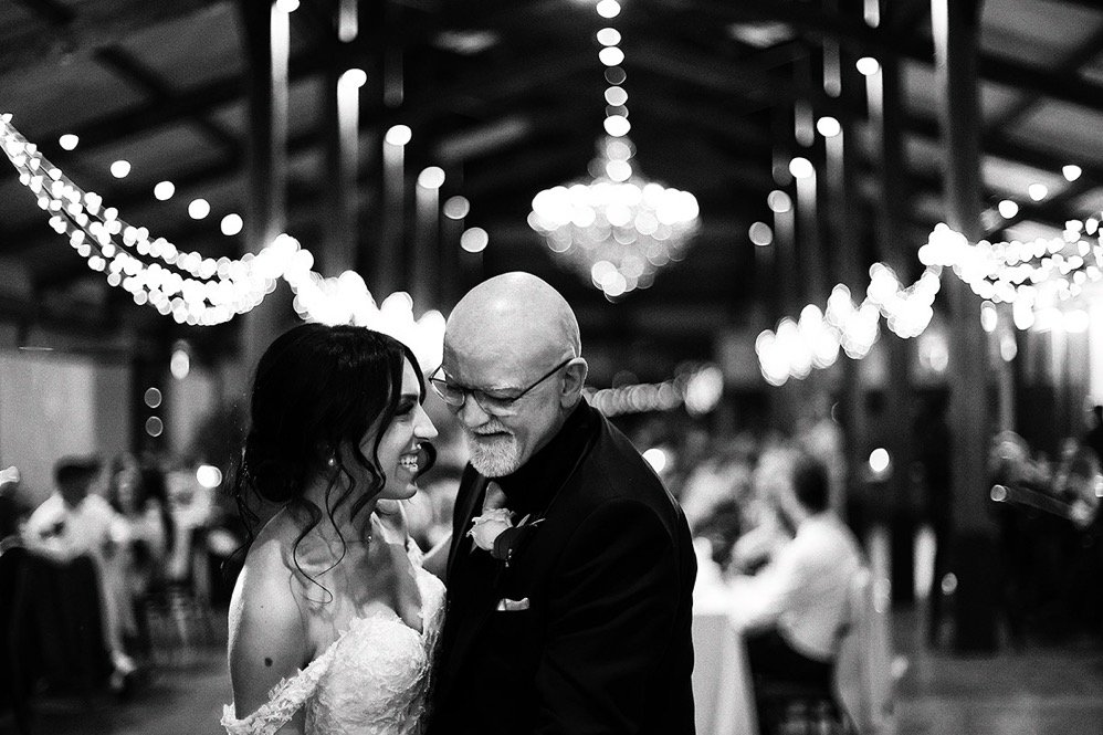 A bride and an older man, possibly her father, sharing a dance at a wedding reception in a decorated banquet hall.