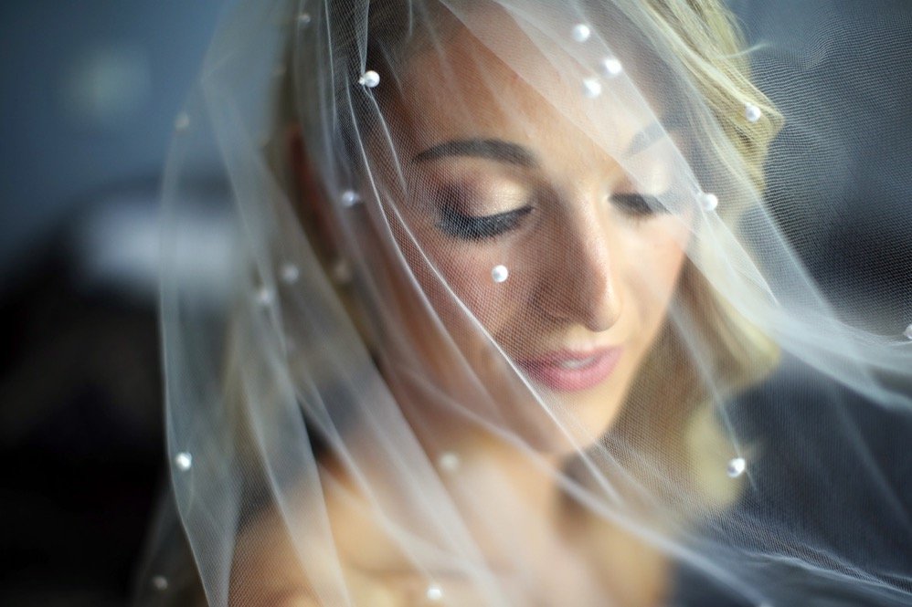 Close-up of a bride with her eyes closed, wearing a veil with small pearl details.