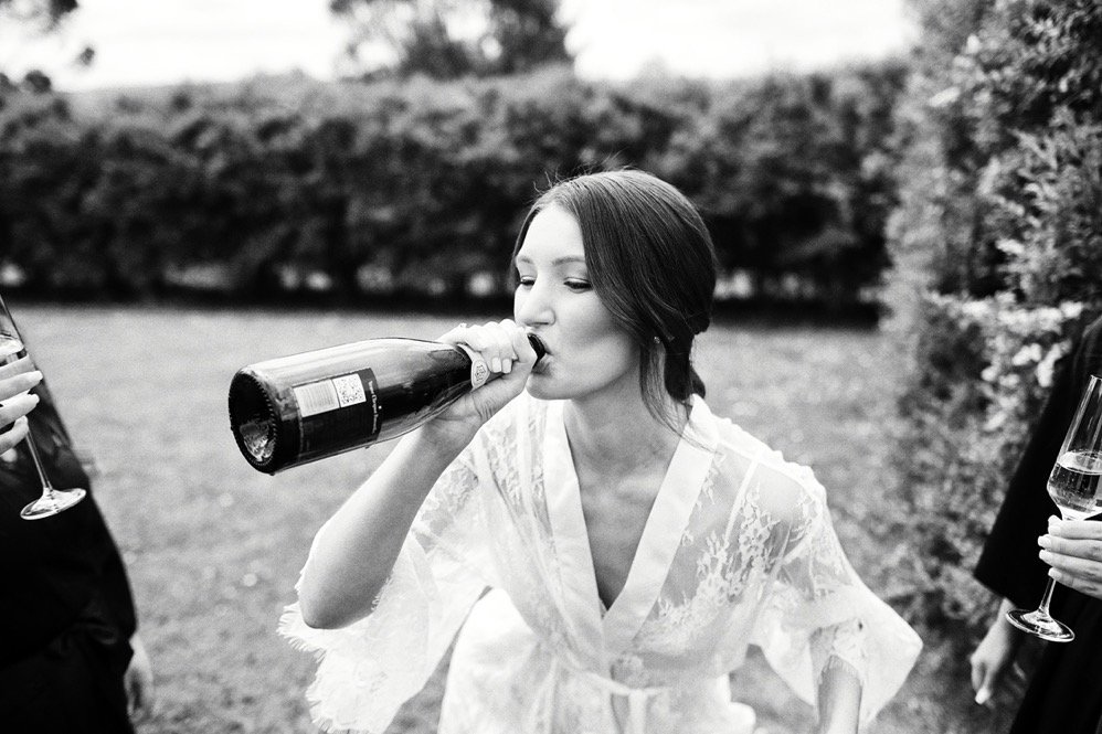 Woman in lace robe drinking champagne outdoors during a celebration or gathering.