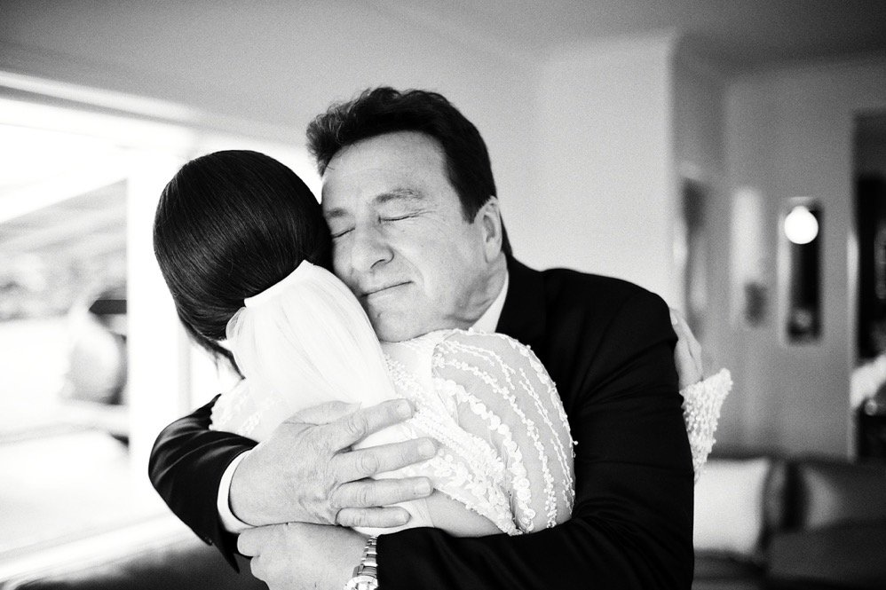 Man and woman hugging warmly, man with eyes closed, in an indoor setting.