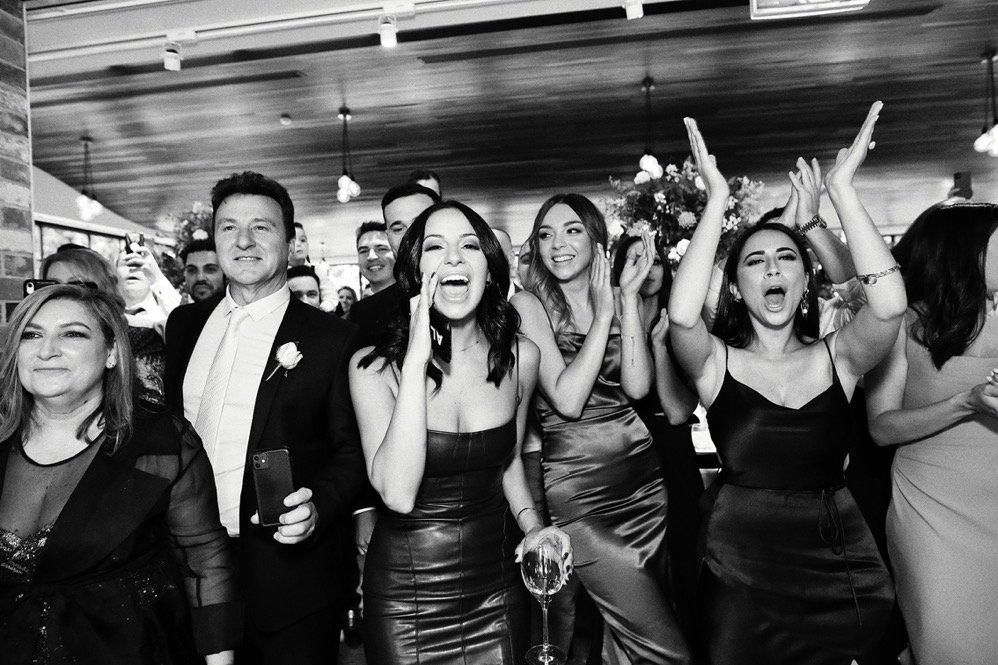 Group of people celebrating at a social gathering or party, dressed in formal attire, smiling, laughing, and clapping.
