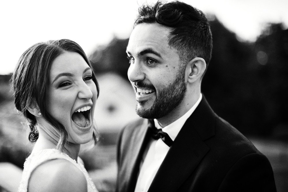 Black and white photo of a happy couple smiling outdoors, dressed in formal attire.