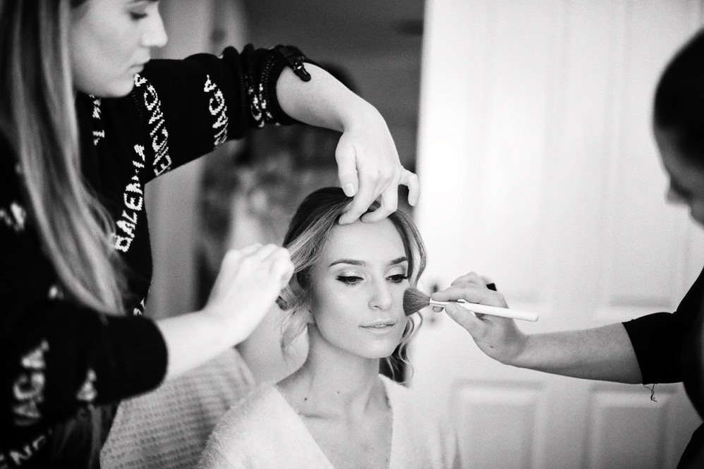 A woman getting her makeup done by two makeup artists in a grooming or dressing room.