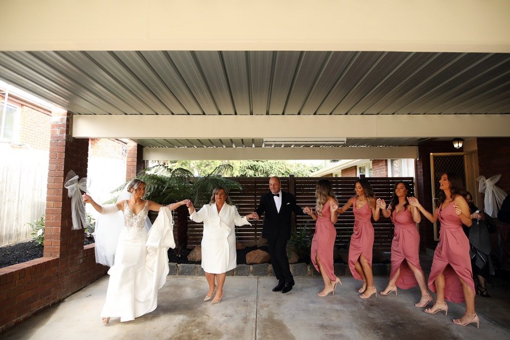 Wedding celebration with bridesmaids and bride dancing in an outdoor covered area.