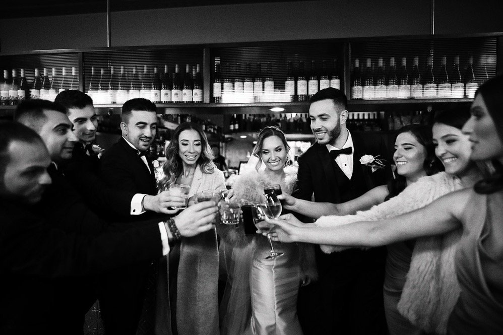 Black and white photo of people celebrating with drinks at a bar, smiling and toasting each other.