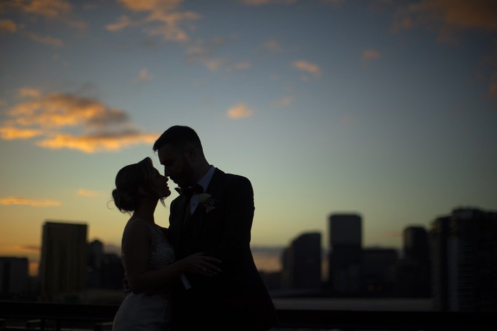 Silhouetted couple embracing against a city skyline at sunset.