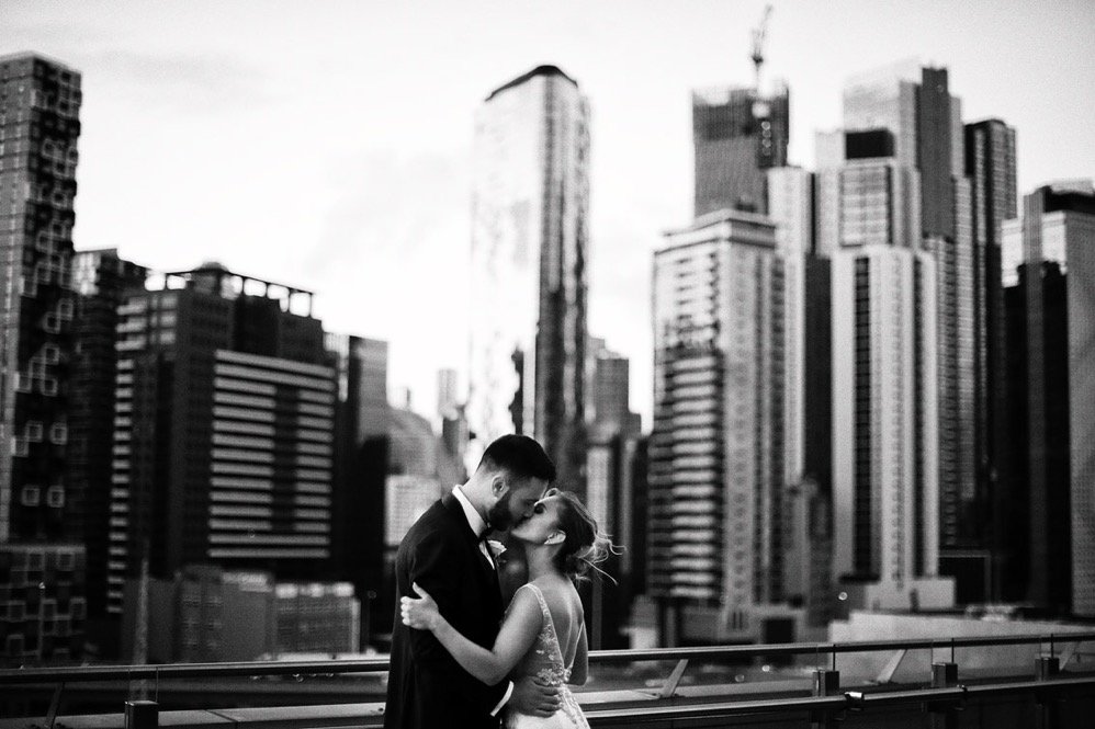 A couple kissing on a rooftop with a city skyline in the background
