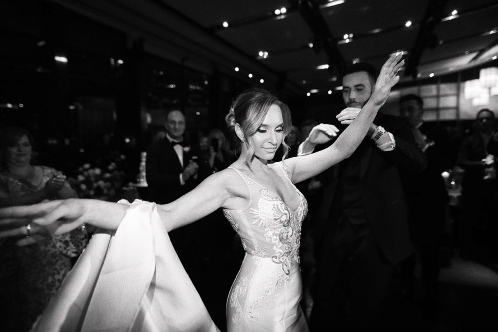 A woman in a wedding dress dancing at a wedding reception, with guests watching in the background.