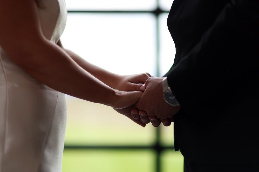 A close-up of a bride and groom holding hands during a wedding ceremony.