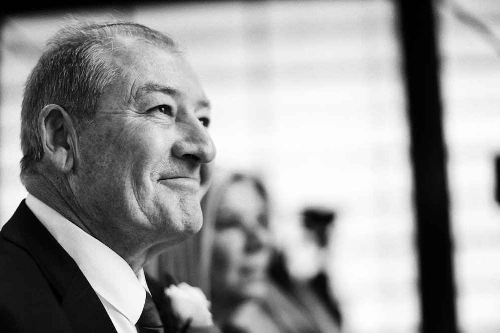 A black and white photo of an older man in a suit, smiling, at a formal event.