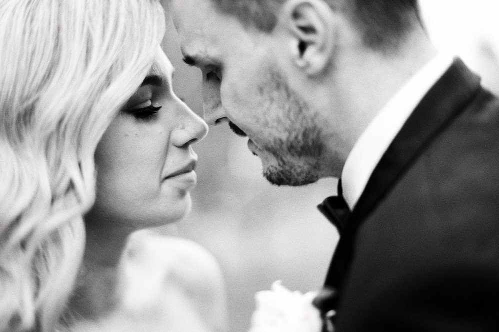 A black and white photo of a man and woman with foreheads touching, close-up, romantic moment, wedding attire, woman with long hair, man wearing tuxedo.