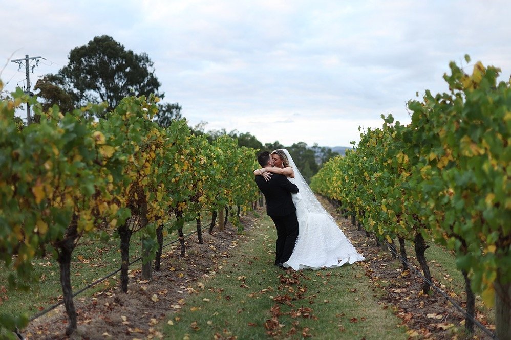 A bride and groom embrace in a vineyard.