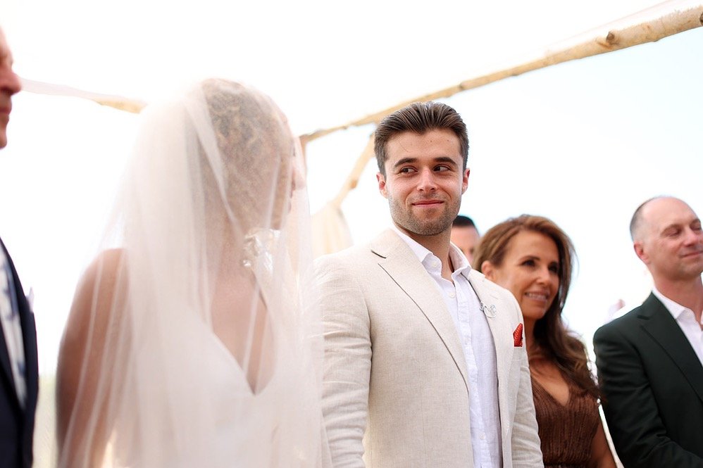 A wedding ceremony with the bride, groom, and guests under a wooden arch.