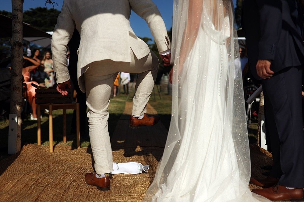 Close-up of a wedding ceremony showing the bride in a white gown and veil, and a groom in a beige suit, holding hands.