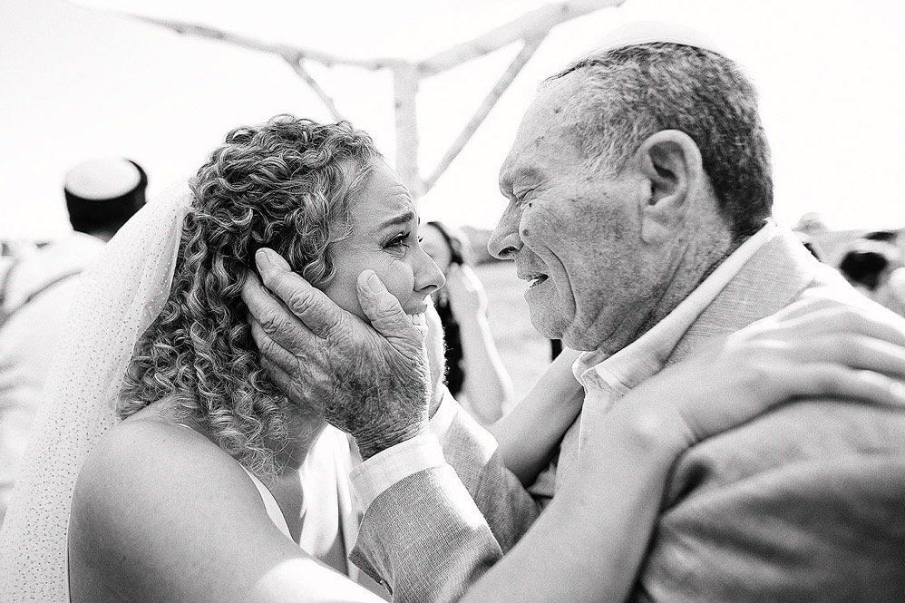 A man and a woman sharing an emotional moment at a wedding, with the man gently holding the woman's face and smiling as they look at each other.