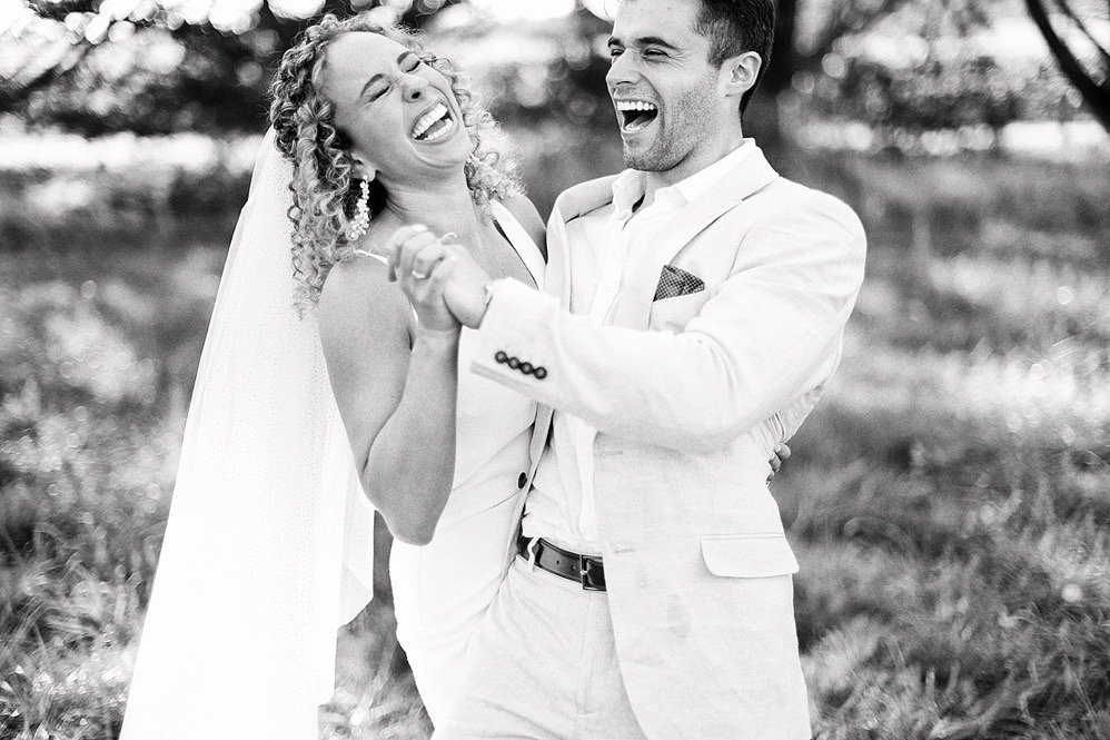 A happy couple in wedding attire dancing and laughing outdoors.