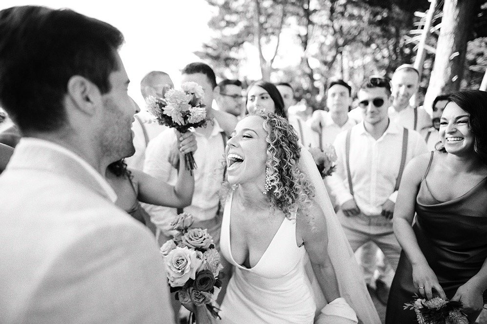 A bride laughing with guests outdoors at a wedding.