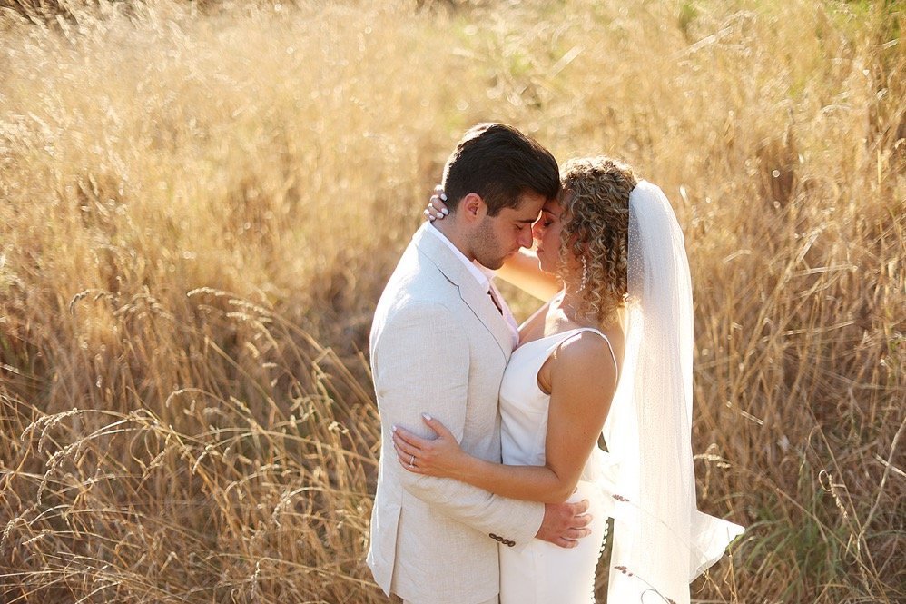 A couple in wedding attire embracing in a field of tall, golden grass.