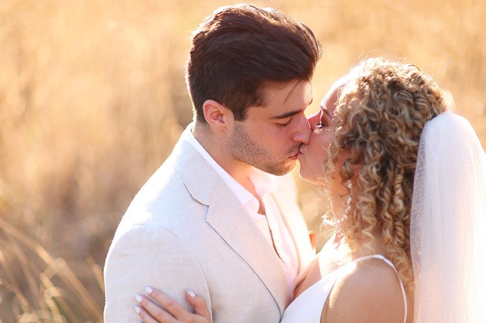 A couple getting married, sharing a kiss outdoors in a warm, golden light.
