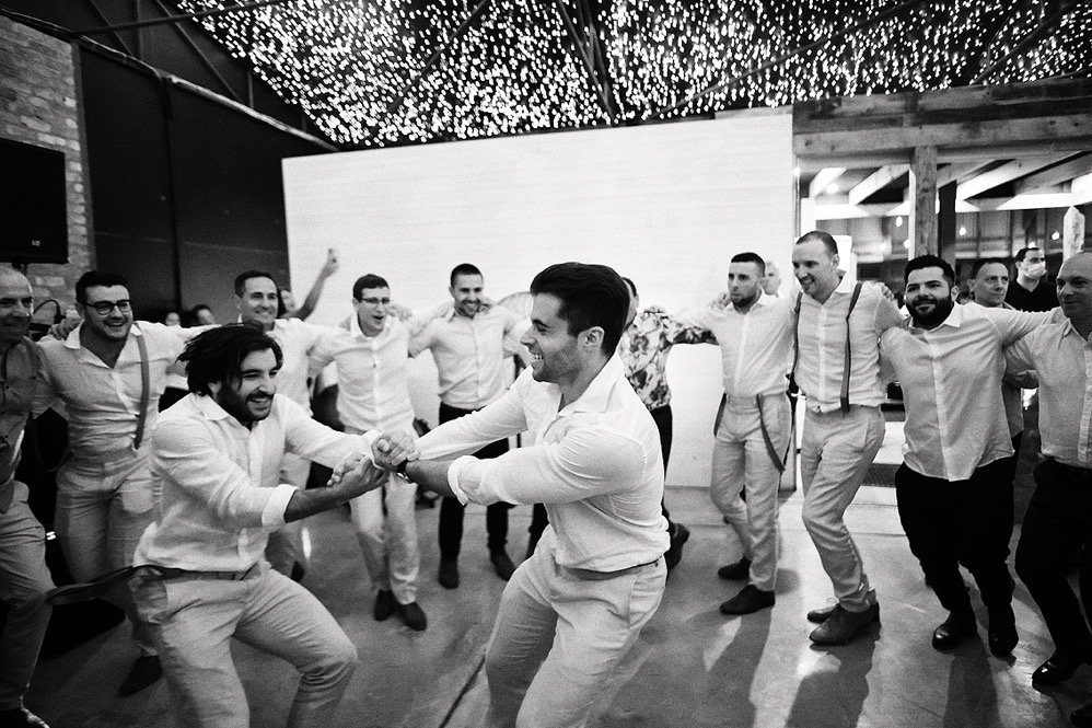 Group of men dancing and celebrating in a circle at a party or wedding reception.