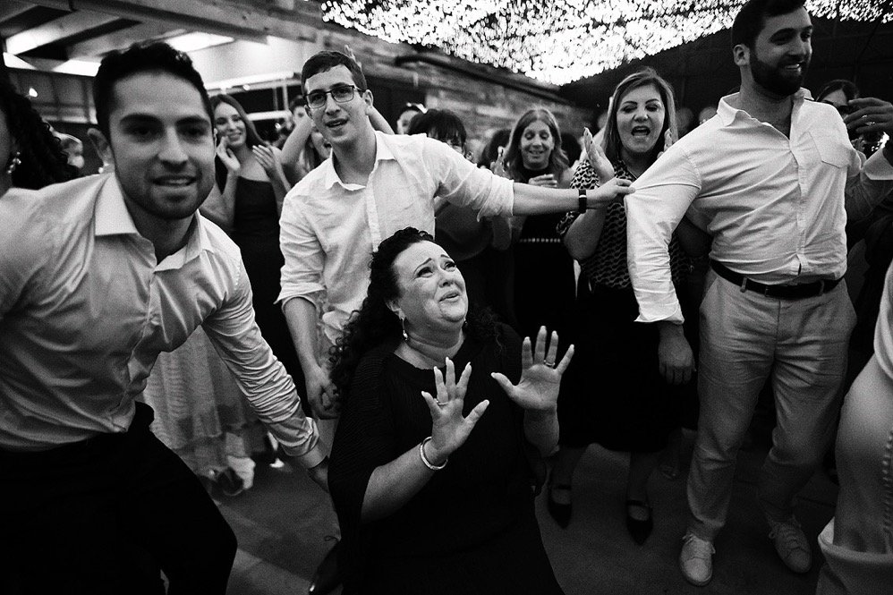 Group of people celebrating at a party or event, with a woman in the center looking emotional and reaching out with her hands.