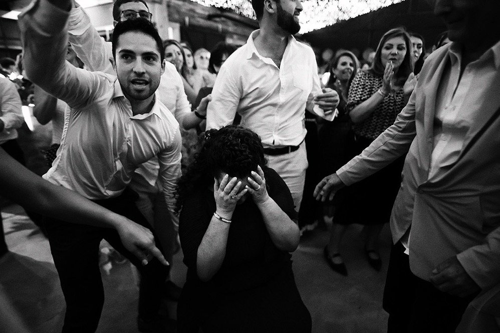 A woman sitting on the ground with her hands covering her face, surrounded by people at a social gathering or party.