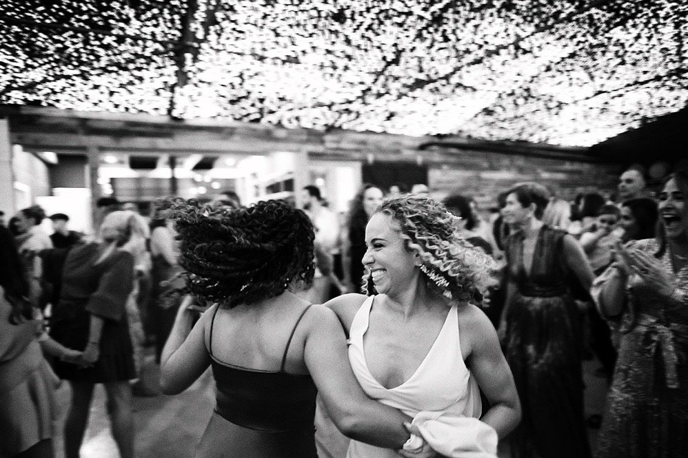 Two women dancing and smiling at a lively indoor party with other guests in the background.