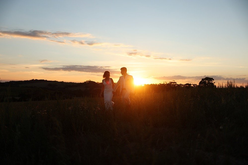 A couple holding hands walking in a grassy field at sunset
