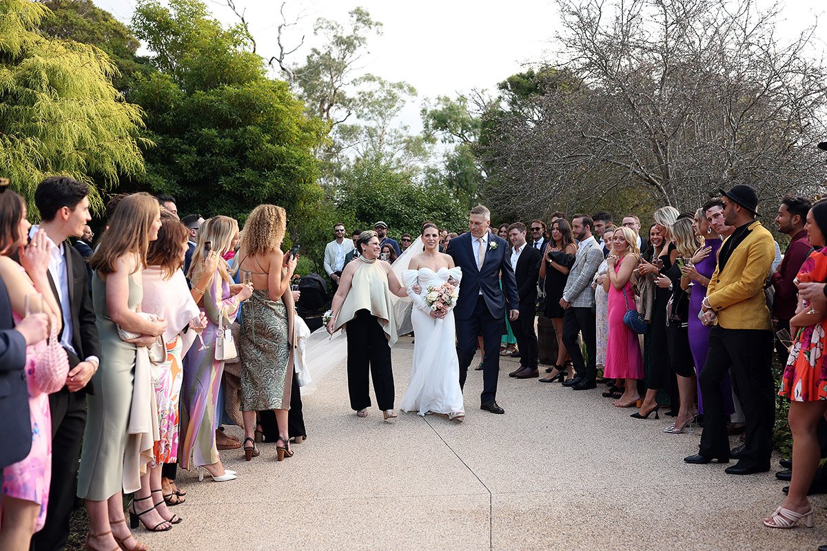 Bride and groom walk between wedding guests lined along an outdoor path.